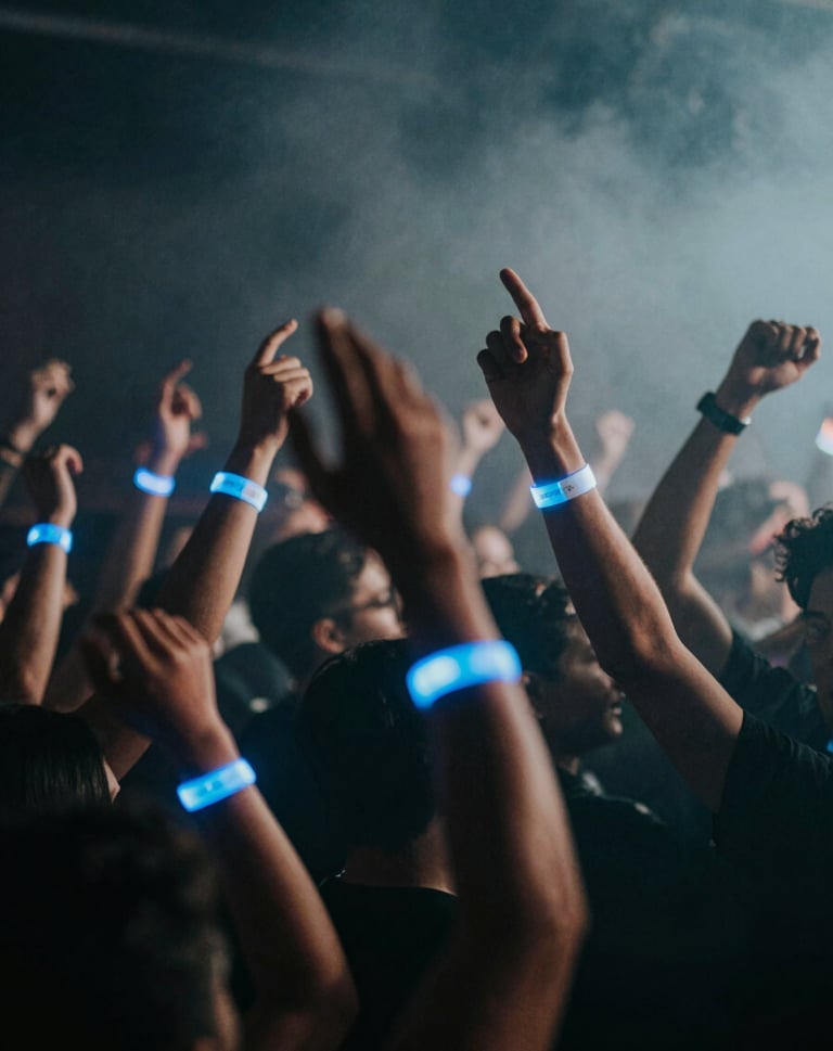 Atmospheric shot of a dancing crowd with hands raised, glowing wristbands in #7A7CF1, hazy smoke, dark nightclub background #0A0A0F.