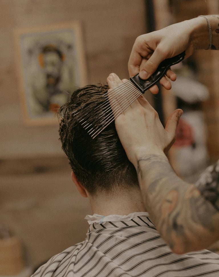 Professional barber using a metal styling pick to shape a man's short haircut in a barbershop.