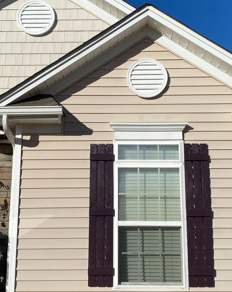 House with two round decorative sections freshly painted white and the shutters freshly painted maroon.