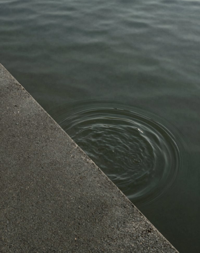 Minimalist abstract photo of water rippling over a textured concrete surface, symbolic of urban water systems, muted charcoal and olive green tones.