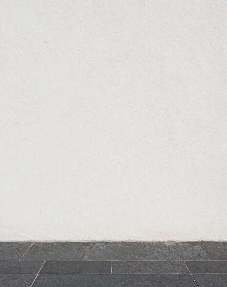 Vertical shot of a white stucco wall meeting a dark gray stone floor, minimal shadow line, editorial architectural detail, clean and sophisticated.