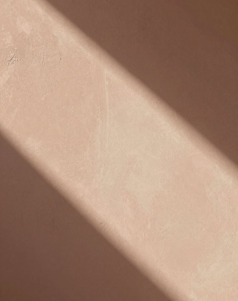An abstract, artistic photograph of soft morning light hitting a textured plaster wall. The shadows are long and gentle. The palette includes dusty terracotta #D1B499 and warm cream #F8F3EC. The composition is minimal and editorial, like a page from an art zine.