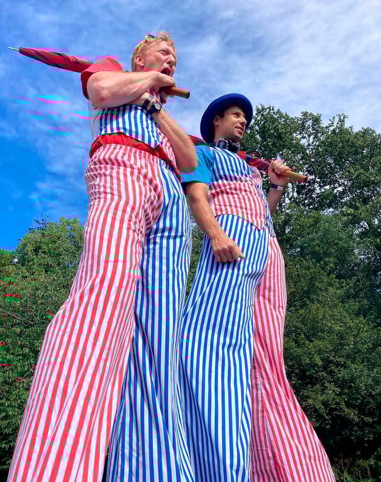 Two circus stilt walkers wearing red and blue striped pants at an outdoor event.
