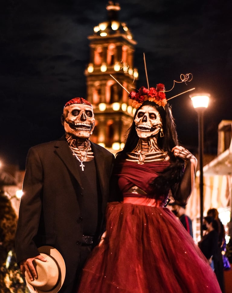 Couple in skull masks celebrating Day of the Dead in front of a Mexican cathedral.