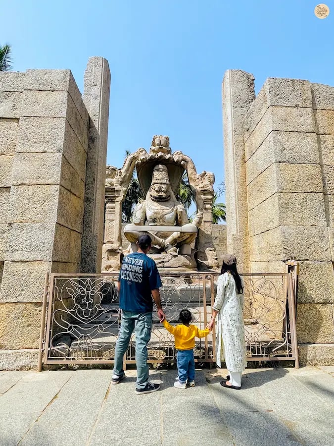 Family beside the Lakshmi Narasimha statue in Hampi, symbolizing divine strength in stone.