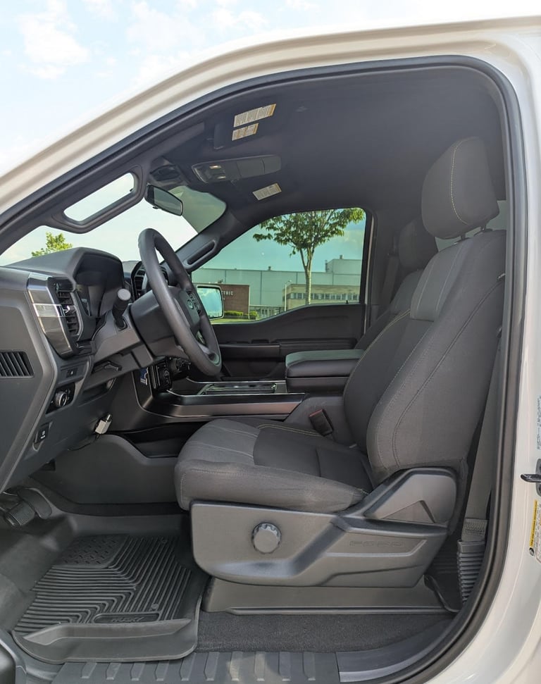 Interior view of a modern white Ford F-150 truck featuring black cloth seats and a leather steering wheel.