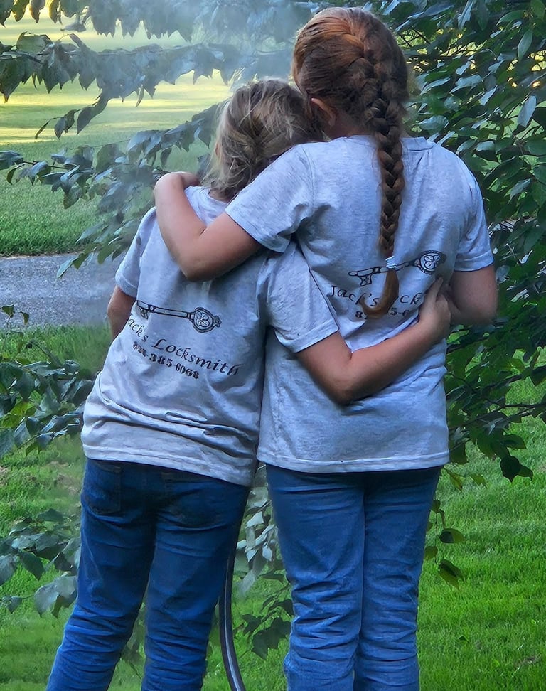 Two daughters hugging outdoors while wearing matching locksmith work shirts