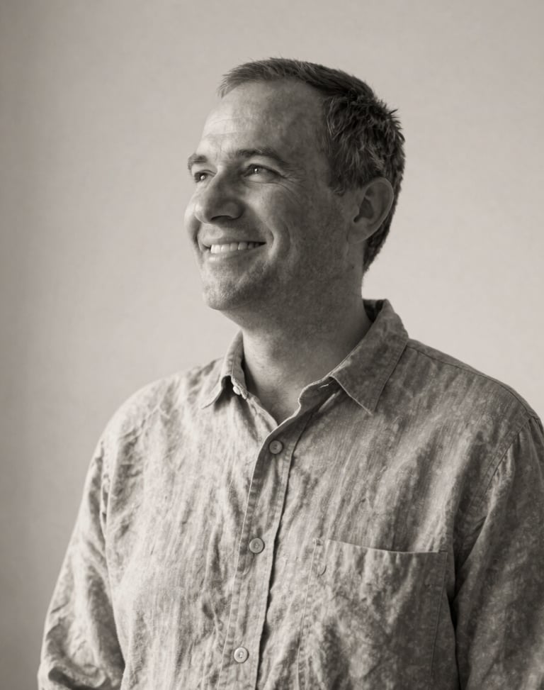 Quiet black and white portrait of a smiling pastor in a simple linen shirt, soft natural side lighting, minimalist background