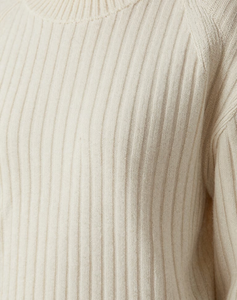 Editorial close-up of women's ribbed wool sweater in bone white, highlighting premium texture