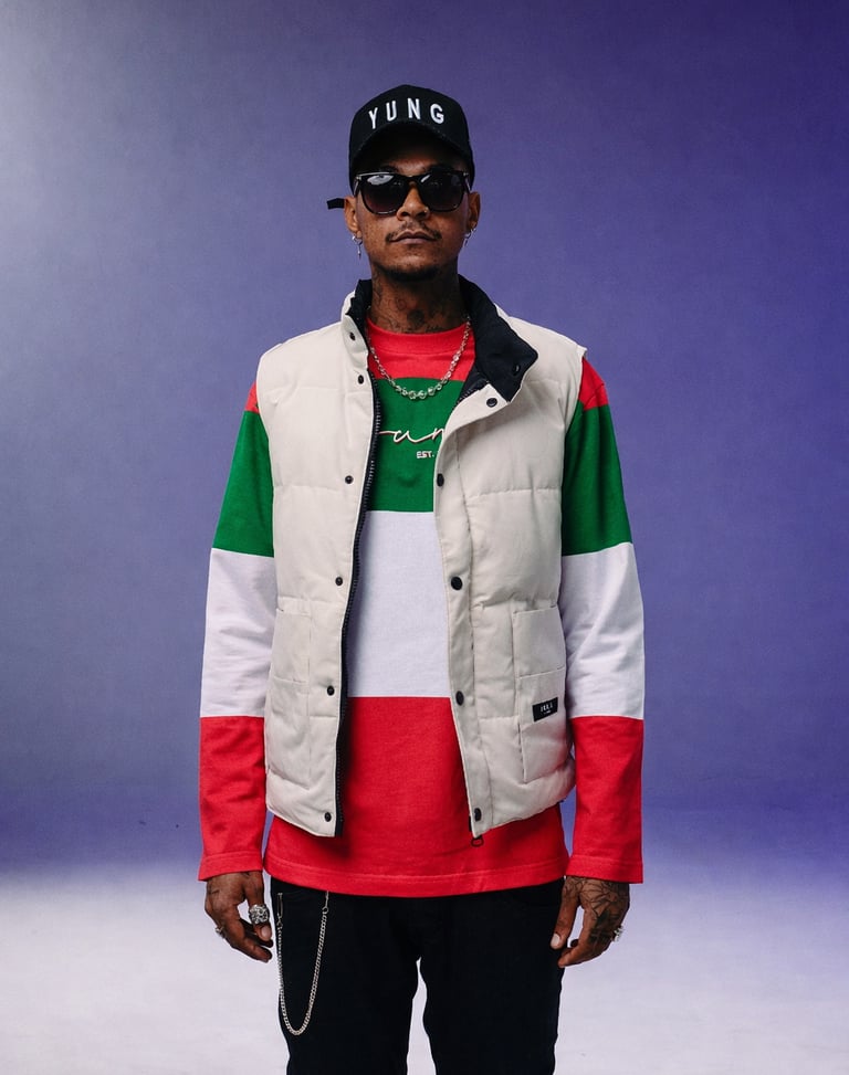 A man in streetwear wearing a cream puffer vest over a green, white, and red striped long sleeve shirt.