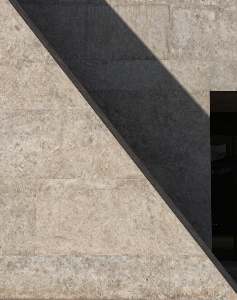 Minimalist architectural geometry of a stone building facade in Madrid, harsh midday shadows cutting diagonally across the concrete panels