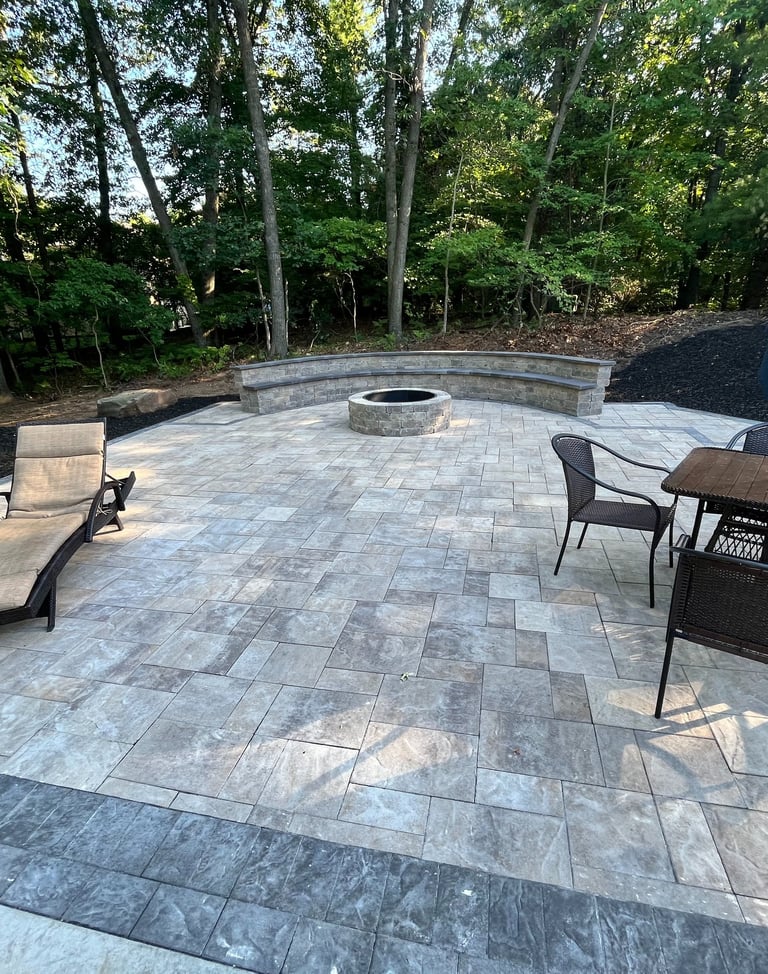 Custom stone paver patio featuring a round fire pit, curved stone bench, and outdoor dining furniture.