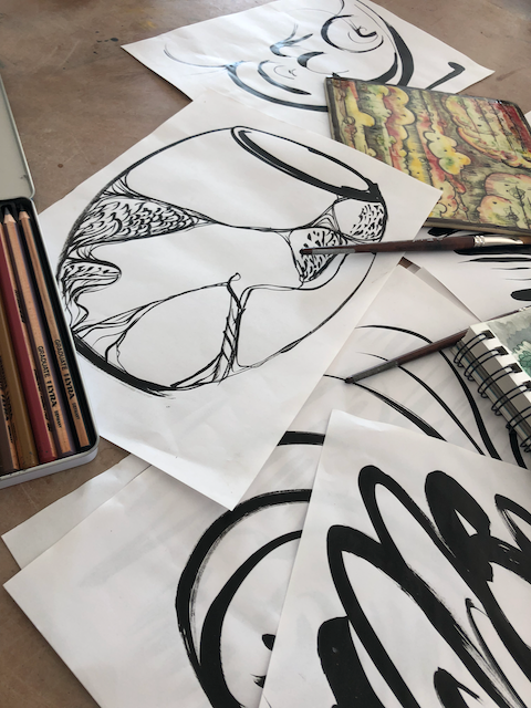 A display of black ink drawings with a vase sketch on top, pencils and notebook