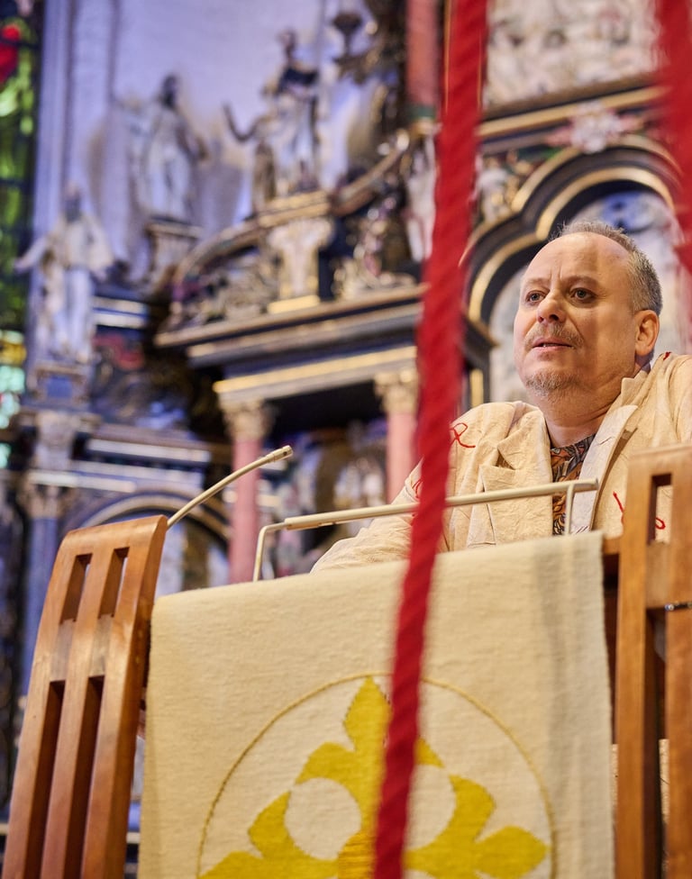 Ein Schauspieler am Rednerpult einer Kirche. Im Vordergrund ein rotes Seil.