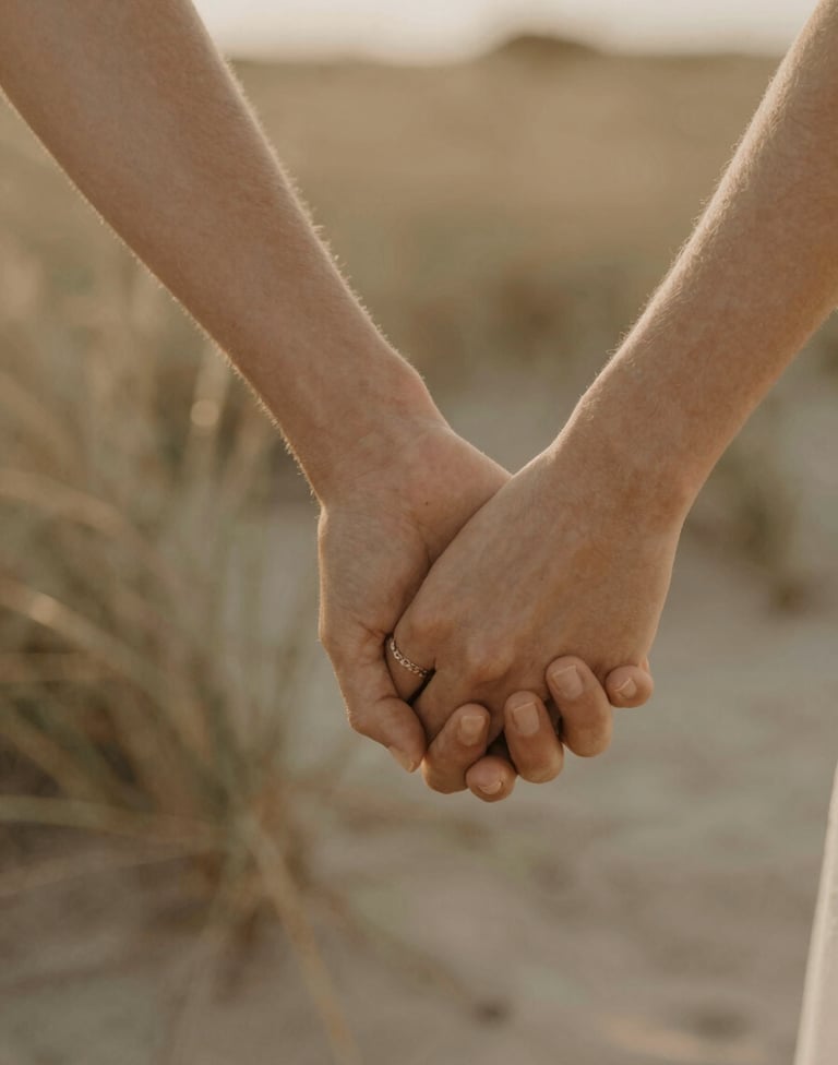 A close-up, intimate shot of a couple's hands gently intertwined against a soft-focus background of dried beach grass, warm golden hour lighting, fine art photography style, incorporating #8F6E5F tones.