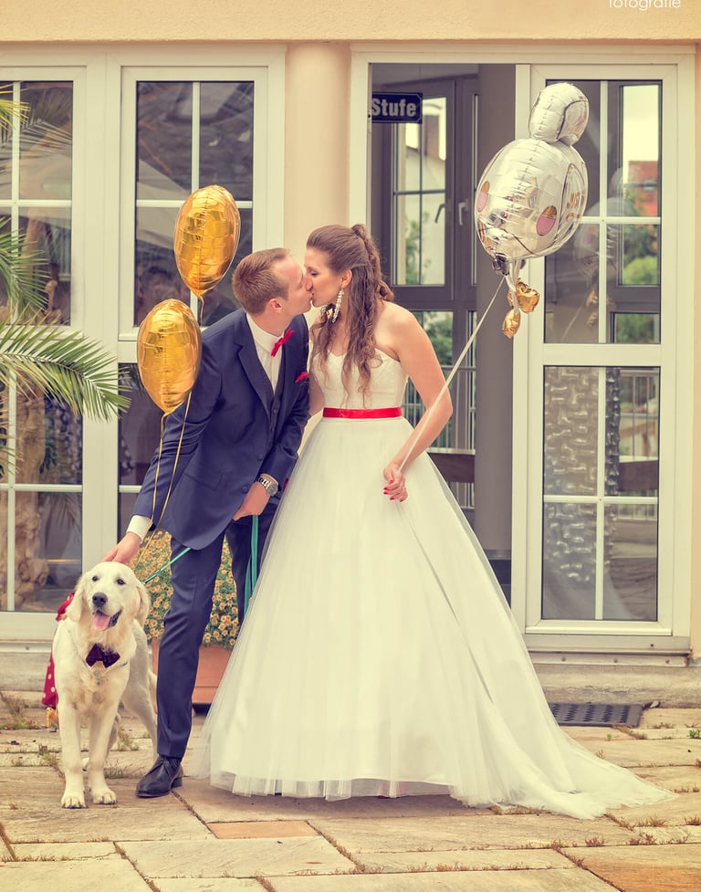 Küssendes Brautpaar mit Ballons und Hund mit Fliege