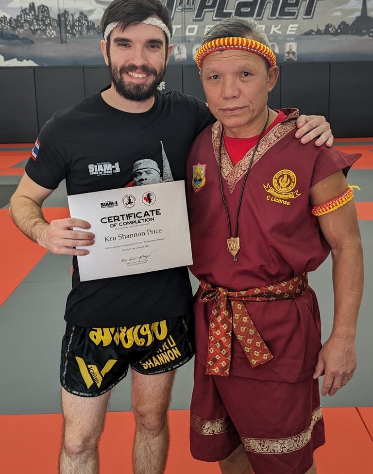 Kru Shannon stands next to Ajhan Suchart after recieving his Kru Certification.