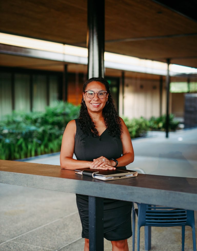 A smiling Lakeland wedding officiant in a black dress and glasses standing in a venue courtyard.