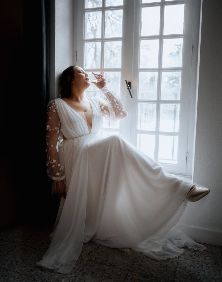 La mariée buvant un verre de champagne au bord d'une fenêtre au domaine de Lamartine