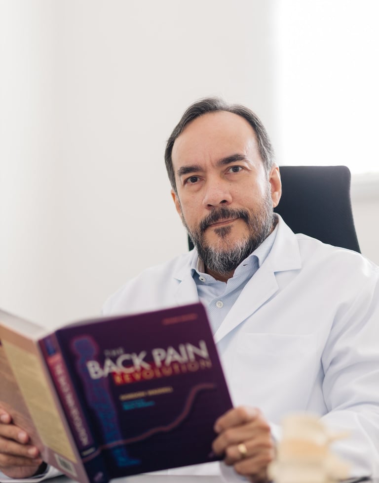 Neurocirurgião Dr. Carlos Moreira especialista em coluna lendo livro sobre dor em consultório.