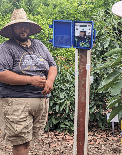 Mira Costa student explaining his water sensor project, standing next to a blue box on a wooden post