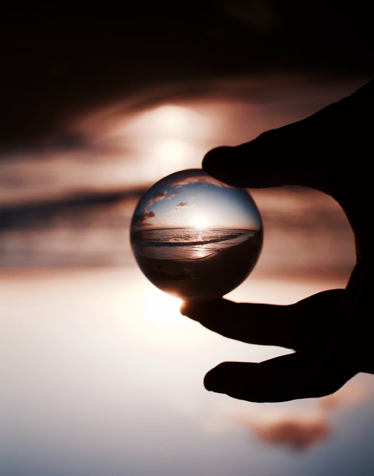 Des doigts tenant une boule de cristal reflétant avec clarté un coucher de soleil sur la mer