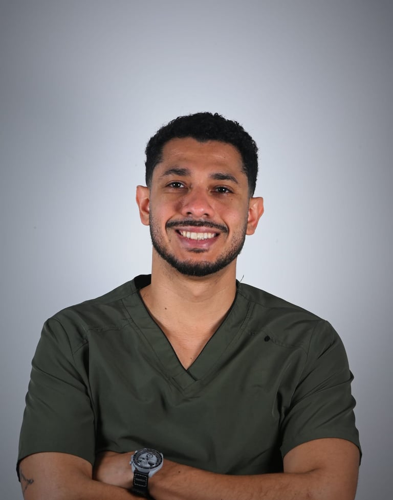A smiling male healthcare professional wearing olive green medical scrubs against a neutral background.