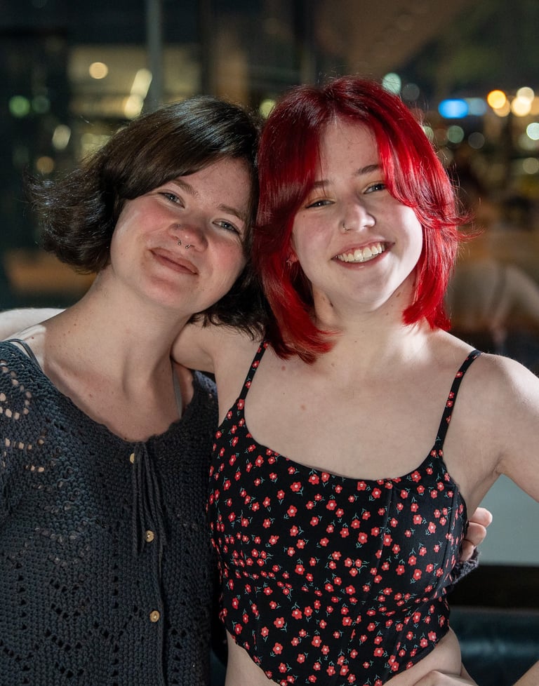 Two smiling young women with short hair and dyed red hair posing together at night.