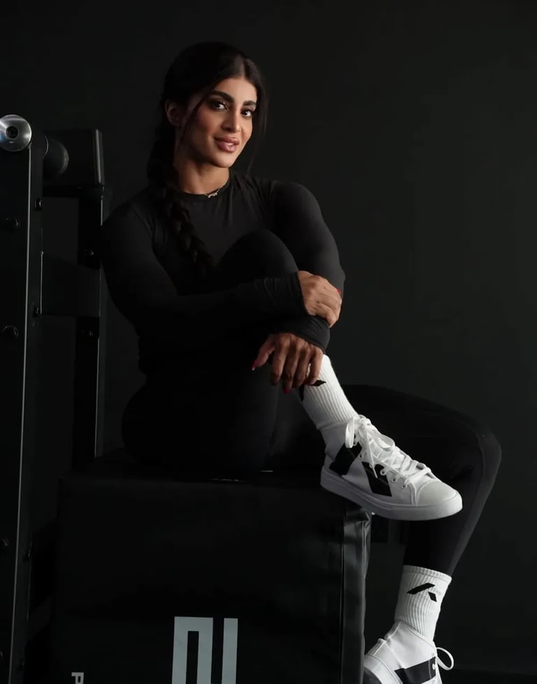 Mais Alhajri in black sportswear and white sneakers sitting in a gym setting, fitness and strength training concept."