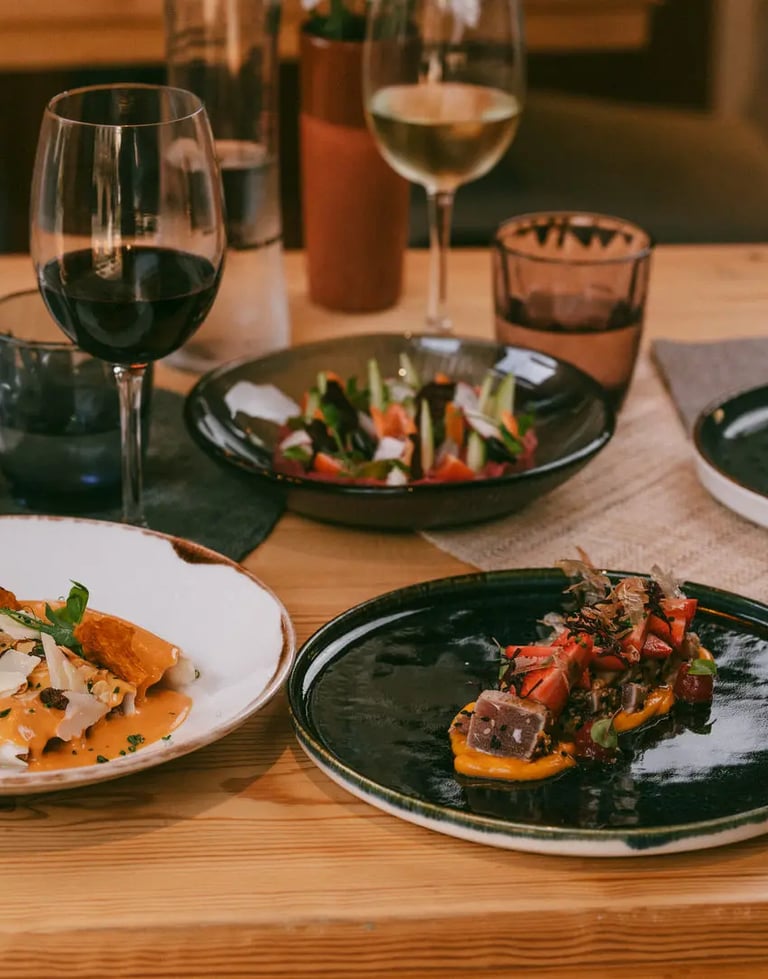 Mesa preparada con varios platos de autor, copas de vino tinto y blanco, y decoración floral en Es Mestral, Ses Salines.