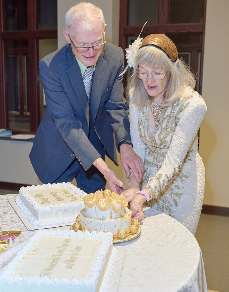 A senior couple celebrates their 50th wedding anniversary cutting a gold and white cake.