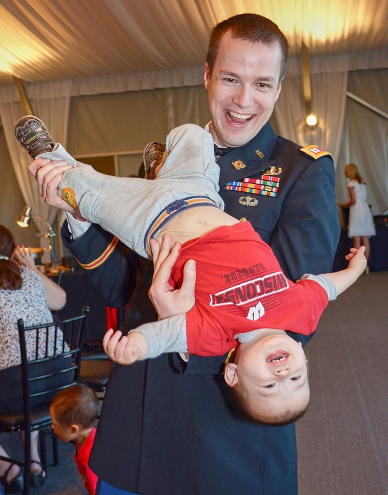 a man in military uniform holding a baby boy upside down in his arms