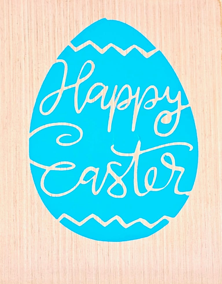 Blue Easter egg sign on a light wood background with cursive Happy Easter lettering.