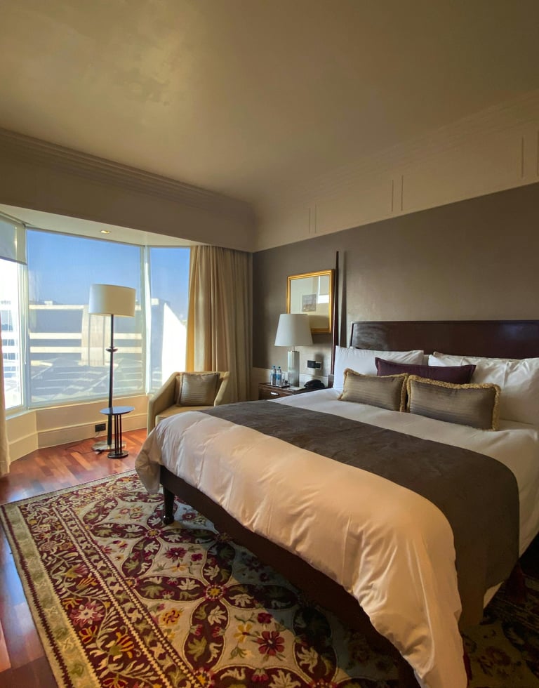 Habitación de hotel con gran ventanal, cama doble y pared marrón