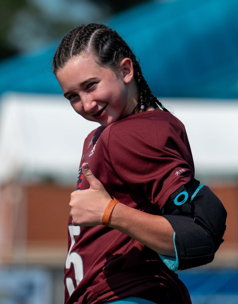 a field hockey goalie in a maroon jersey shirt is smiling and giving a thumbs up
