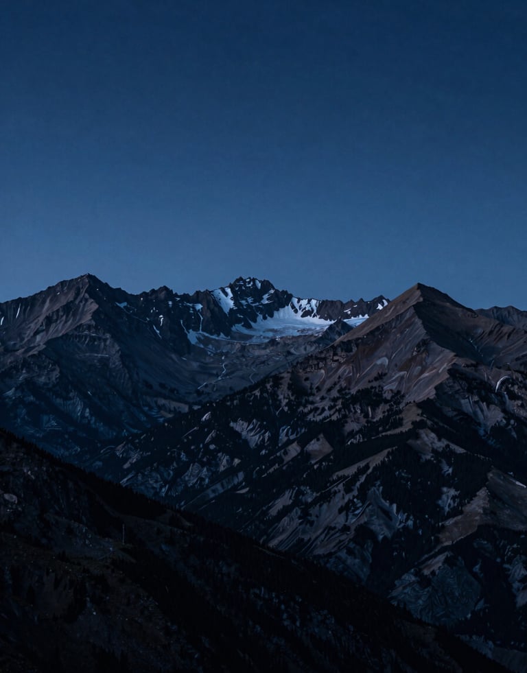 A wide-angle shot of the Pyrenees mountain range at dawn. The peaks are silhouetted against a deep midnight blue sky with hints of soft steel blue light on the ridges. Atmospheric and serene.