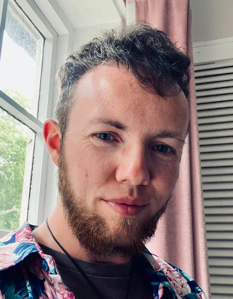 White trans masc with blue eyes, and curly light brown/auburn hair and beard. 