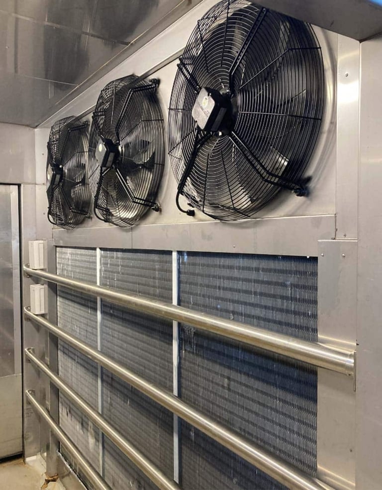 Industrial evaporator unit with three large fans and cooling coils inside a commercial walk-in freezer.