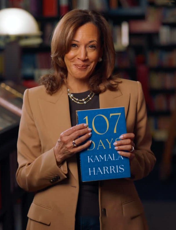 Smiling VP Kamala Harris holding her new book, 107 DAYS.