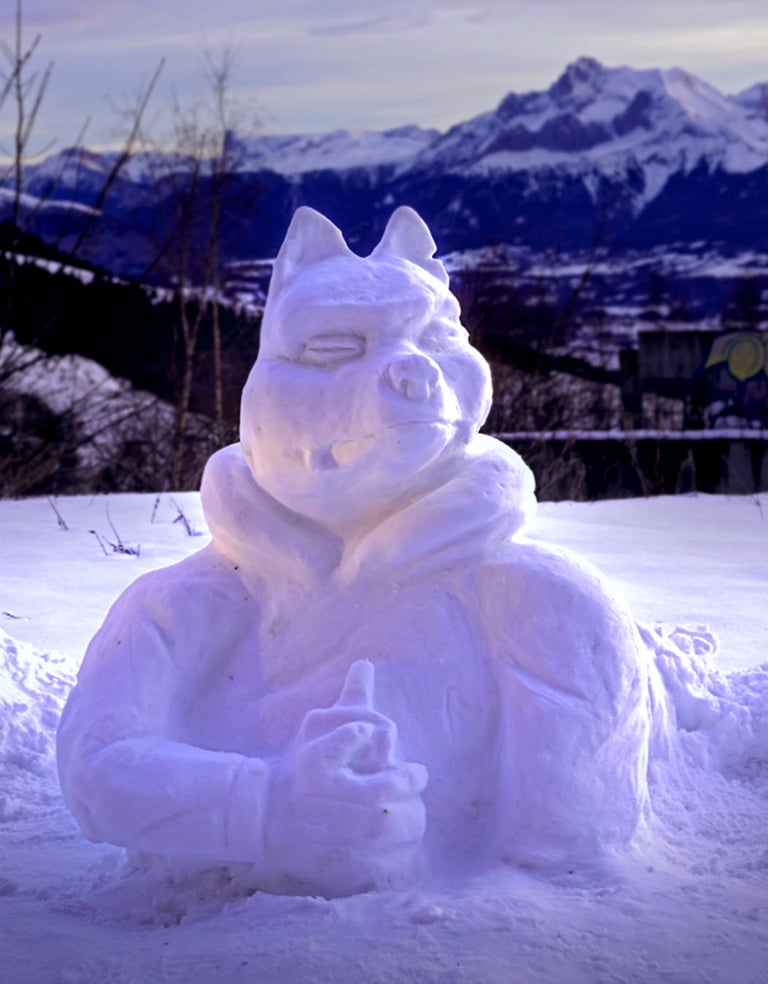 A creative snow sculpture of a cartoon character with mountain peaks in the background.