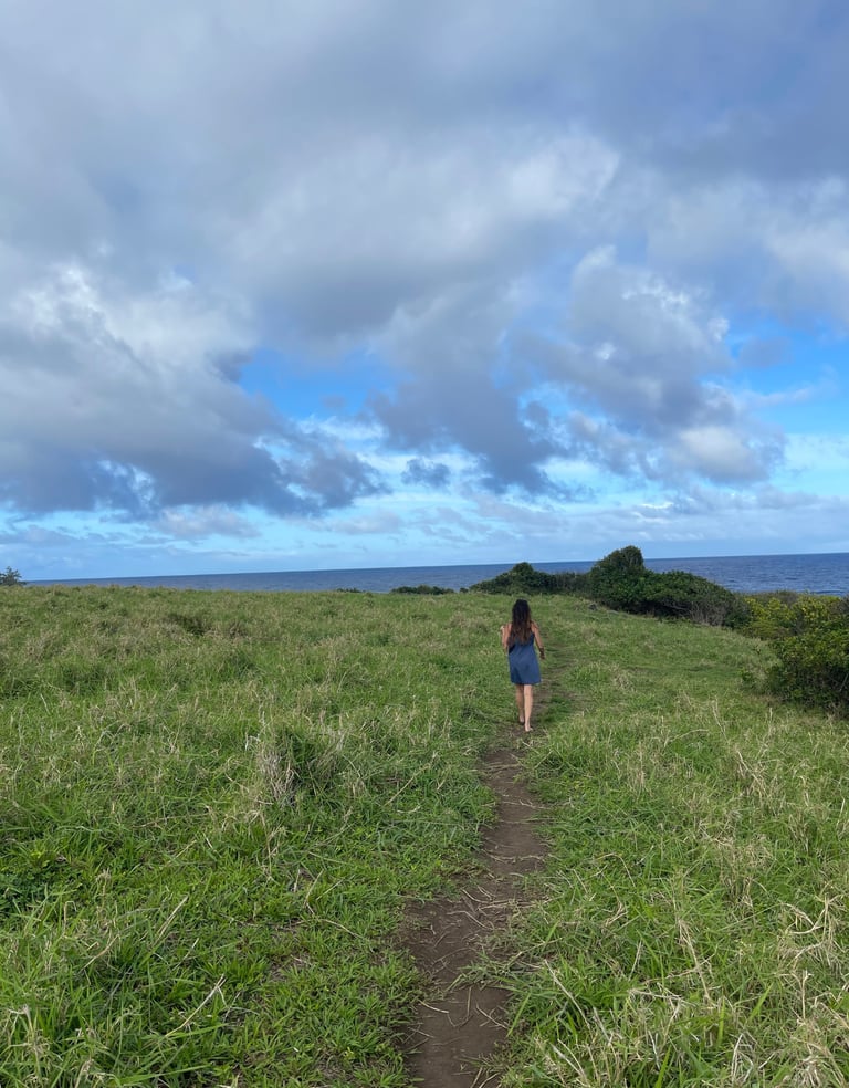 A woman walking away down a cliffside path on a Hawaii ocean cliff