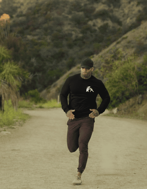 Hombre atlético trotando al aire libre, vistiendo una camiseta negra de manga larga y cachucha.