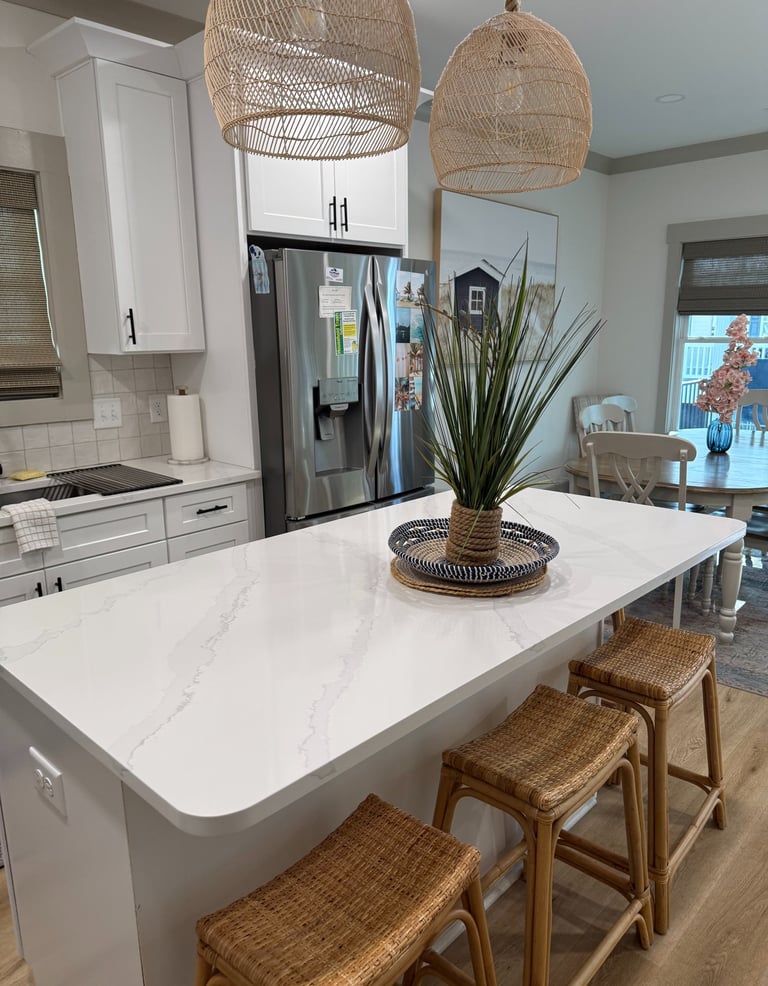 Modern white kitchen featuring a quartz island with wicker bar stools and rattan pendant lights.