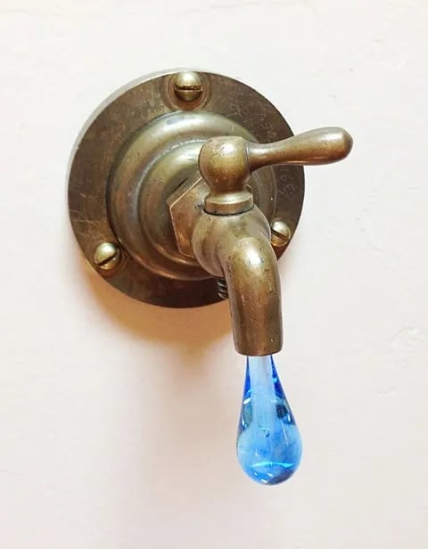 Vintage brass faucet with light blue glass drip coming out ot the spout.