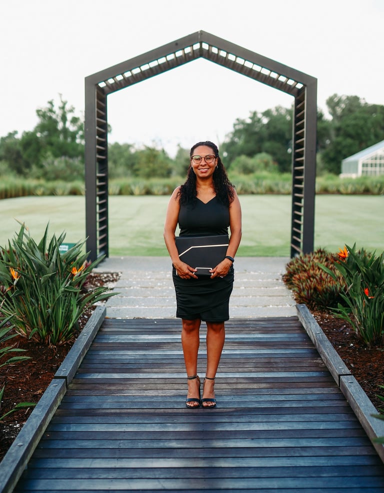 Professional woman in black dress holding folder at outdoor garden event venue.