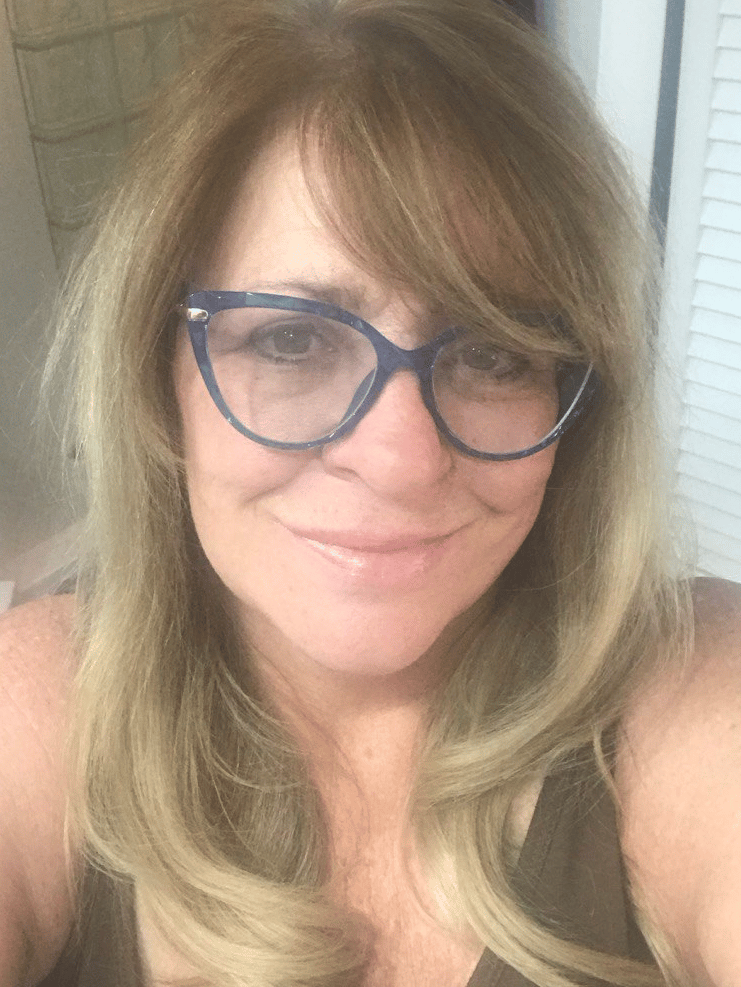 A smiling woman with blonde hair wearing stylish blue cat-eye glasses.