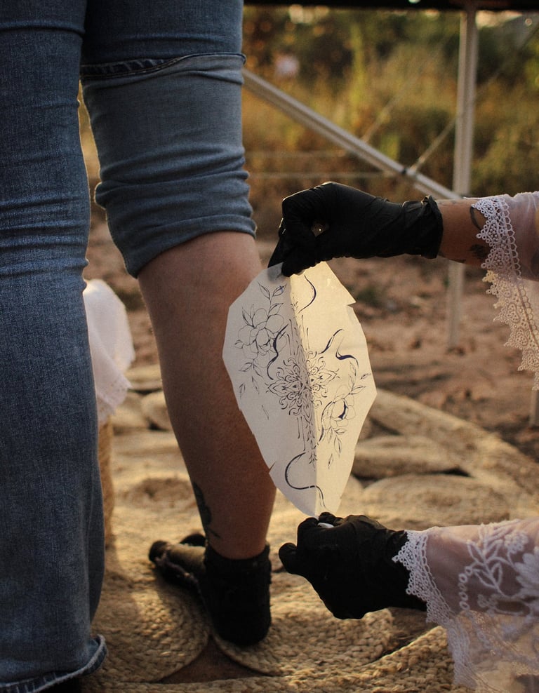 un calque de tatouage est posé sur un mollet, dans une ambiance aux couleurs chaudes
