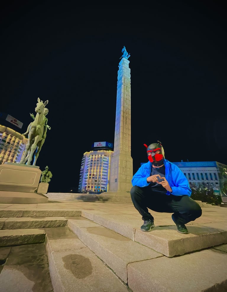 A man in a pup mask posing by a monument at night.