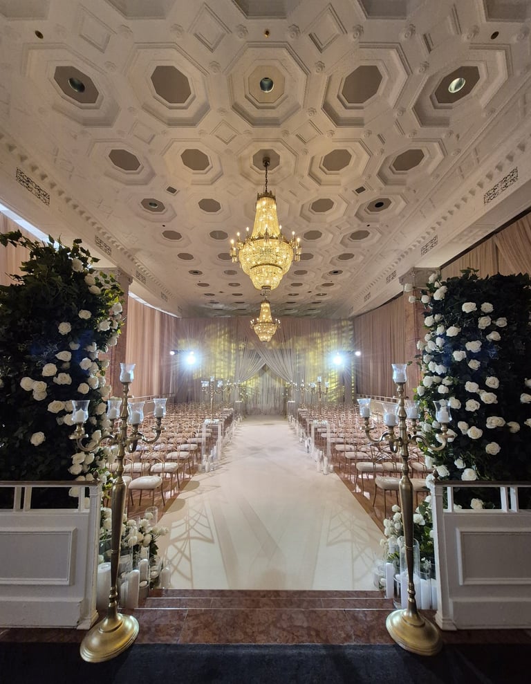 Elegant wedding ceremony setup in a grand ballroom with chandeliers, floral arches
