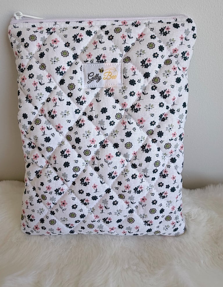 Quilted floral book sleeve with a zipper, featuring pink and green flowers on white fabric.
